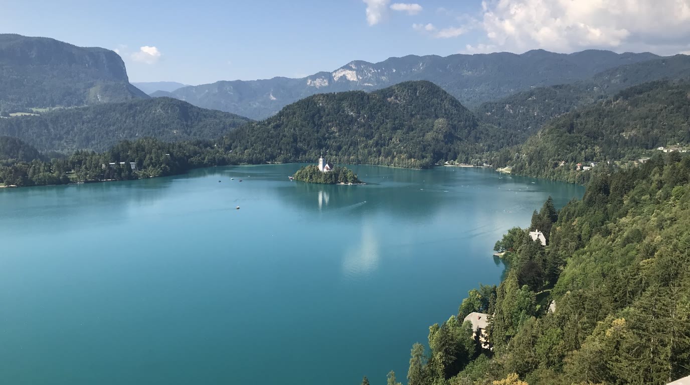 Lake Bled with its island and little church, a castle on a cliff above the water and the ridges of the Julian Alps in the background