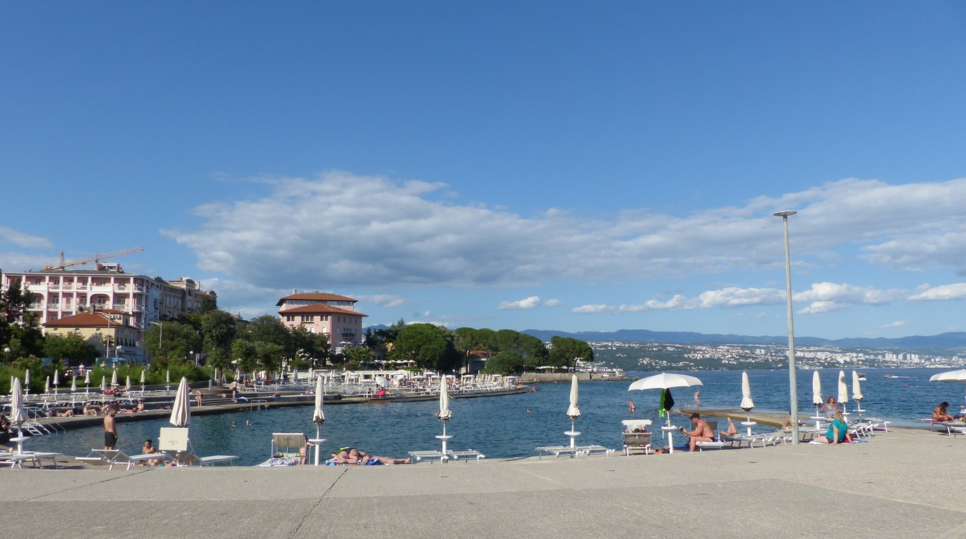 A motorhome on a coastal road above a bay in the Kvarner, with the sea, pine trees and an island in the background