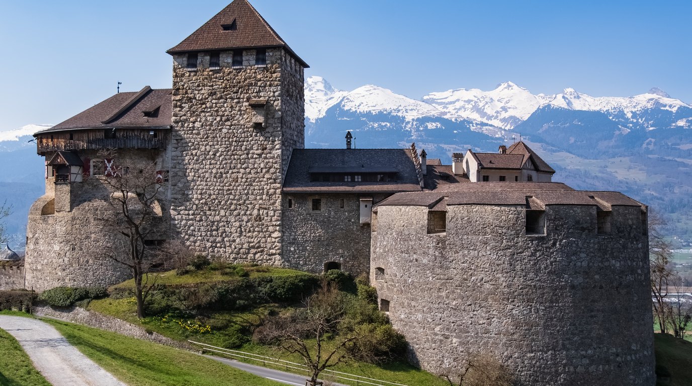 Zámek Vaduz na skalním ostrohu nad hlavním městem Lichtenštejnska, v pozadí alpské hřebeny