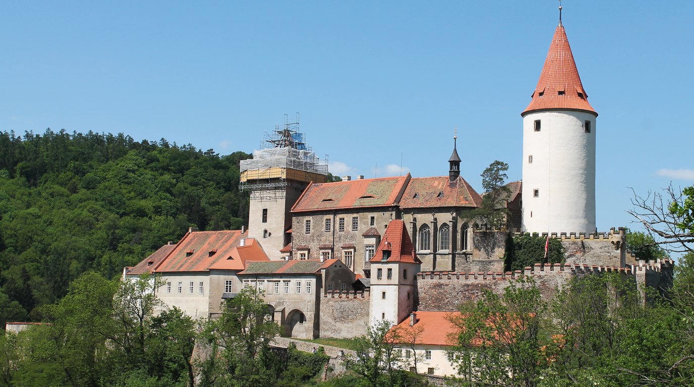 Hrad Křivoklát s vysokou válcovou věží nad zalesněným údolím Berounky