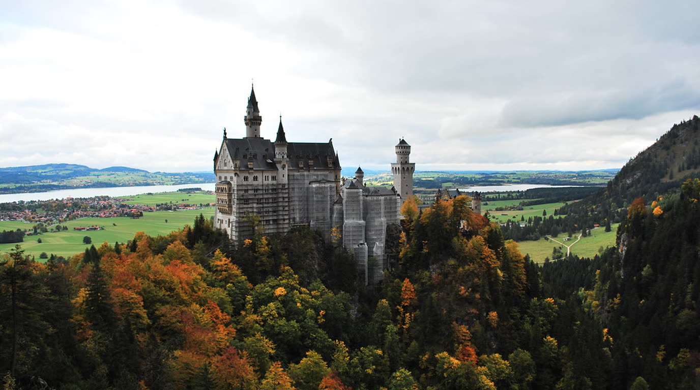 Zámek Neuschwanstein na skalním ostrohu nad údolím, v pozadí hřebeny Bavorských Alp